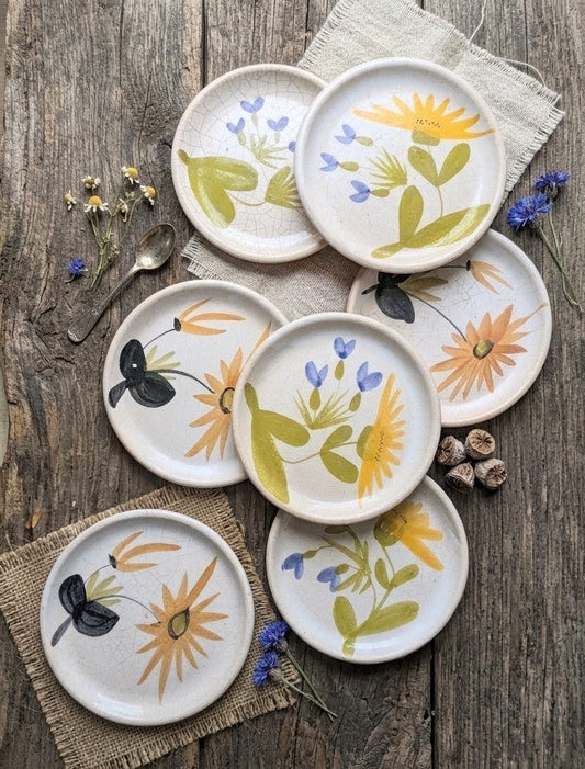 Ensemble d'assiettes à dessert artisanales en grès émaillé de la Poterie du Marais, peintes à la main avec des motifs de fleurs jaunes et bleues sur fond crème craquelé, style rustique et vintage.