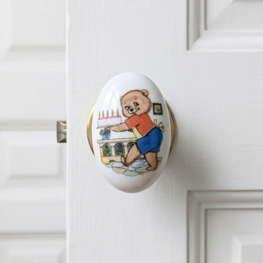 poignée de porte ovale en porcelaine blanche avec une illustration vintage en couleur d'un ourson tenant un gâteau d'anniversaire avec des bougies.