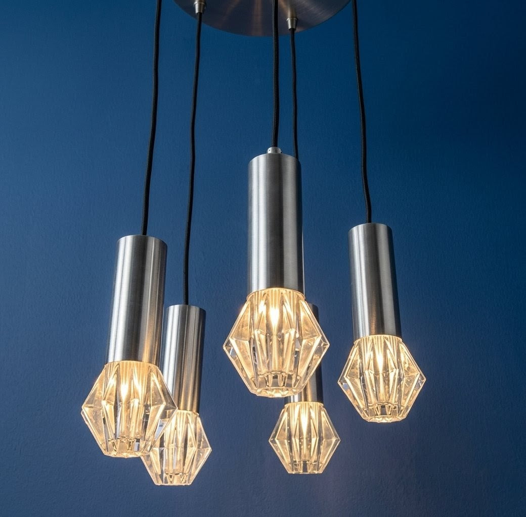 suspension cascade vintage à cinq feux, style Mid-Century modern. Cinq diffuseurs géométriques imitant des diamants, sont suspendus à différentes hauteurs par des câbles noirs reliés à un support de plafond circulaire en métal chromé brossé. 